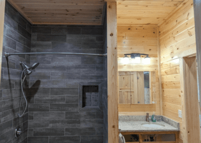 A bathroom with wood-paneled walls, a shower area with dark tiles, a bathtub, and a sink with a mirror under recessed lighting.